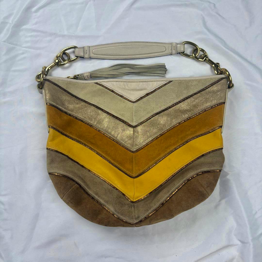 Top-down front view of the COACH one-shoulder multicolor suede and leather bag showing chevron color panels, tassel, and shoulder strap on a white background.
