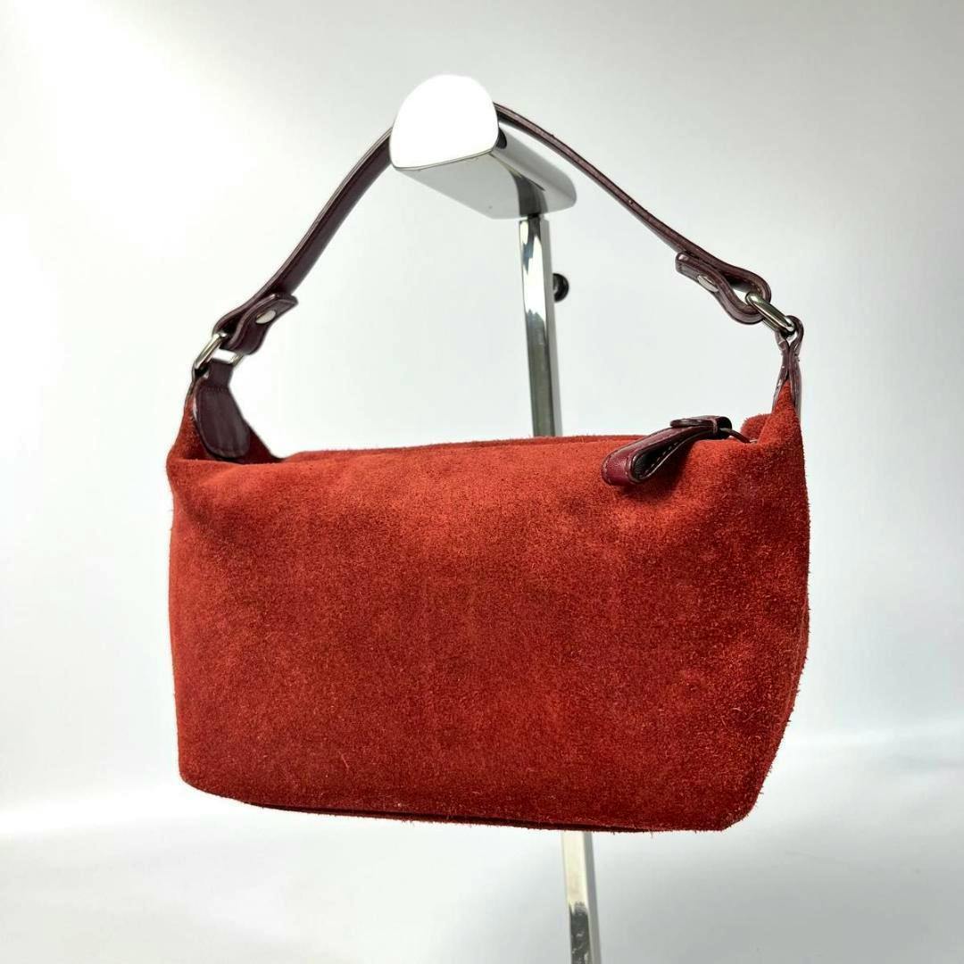 Red suede shoulder bag with a short leather strap hanging on a display stand.