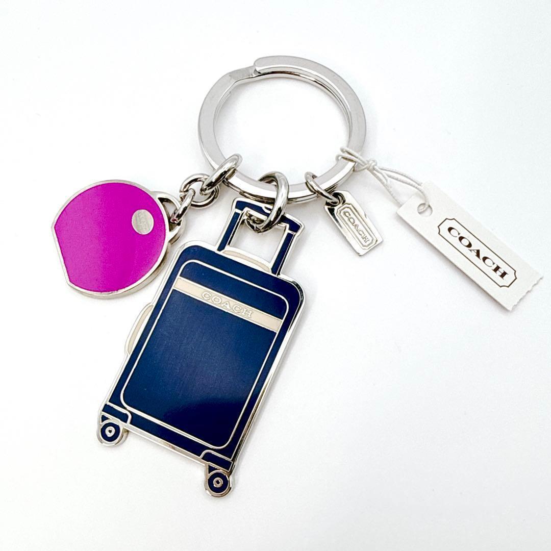 A Coach suitcase-shaped key charm with a pink round tag, metal key ring, and Coach logo hang tag on a white background.