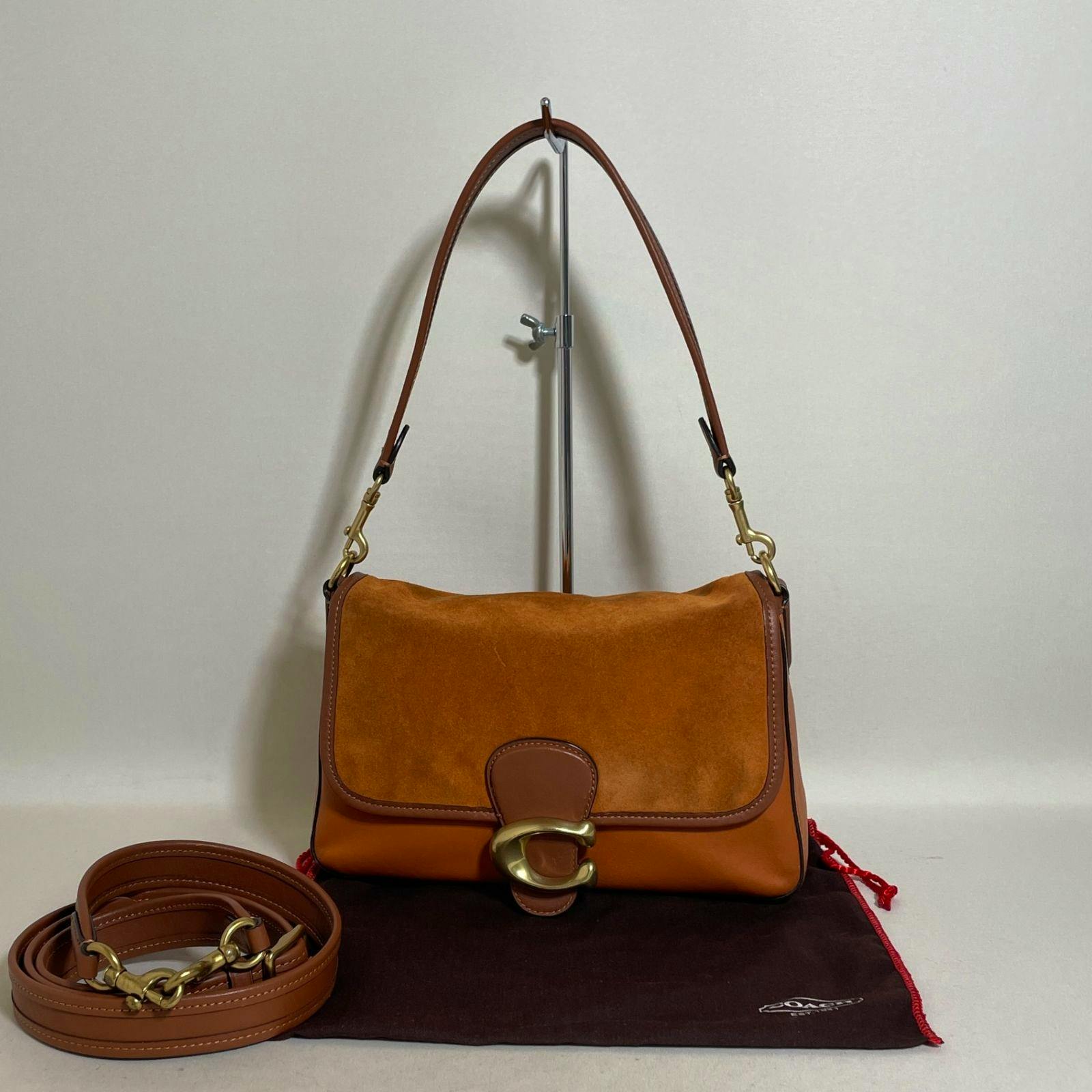 Front view of a brown Coach Tabby 2-way leather and suede bag with shoulder strap and an additional strap placed on a dust bag.