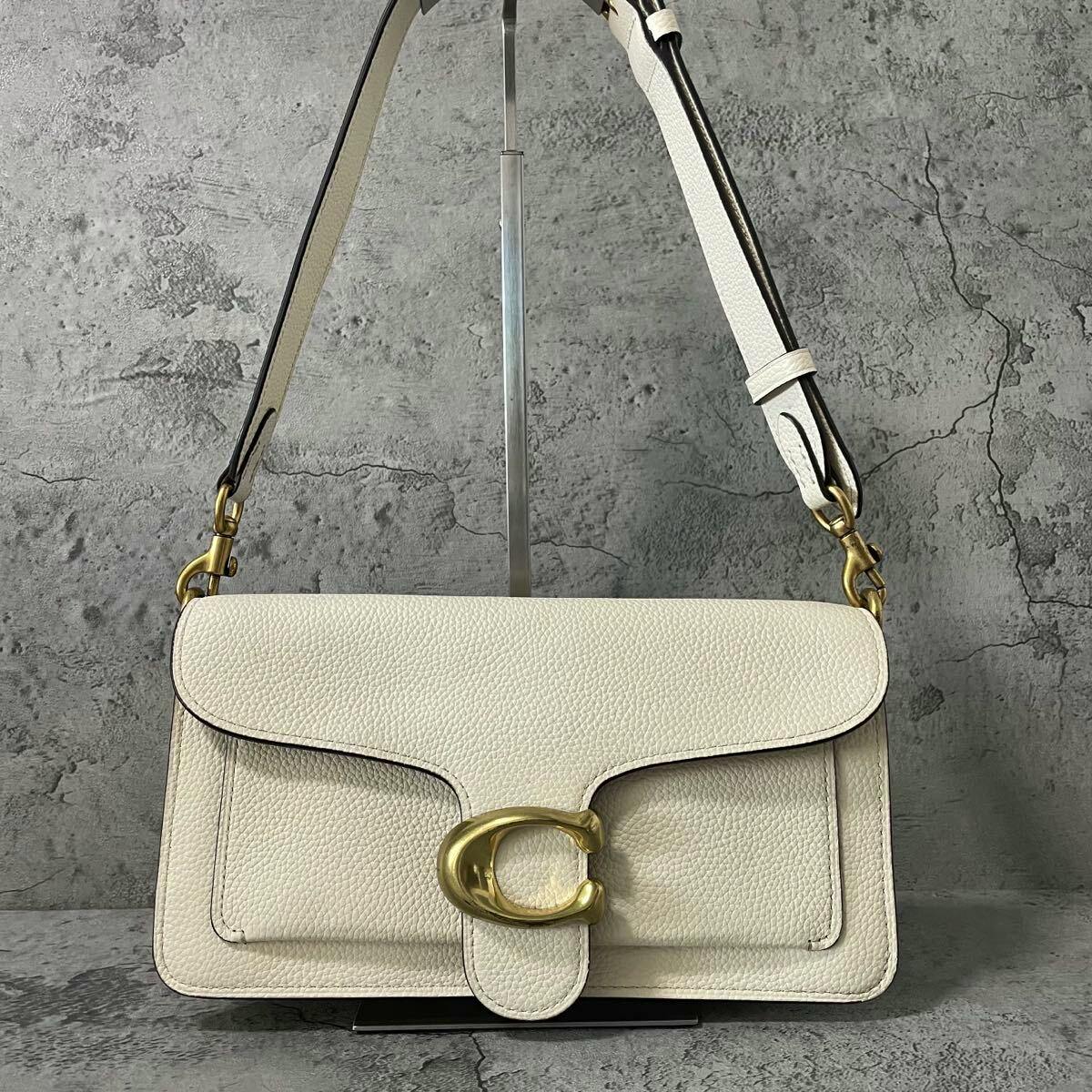 Front view of a white Coach Tabby leather shoulder bag with a gold C clasp and adjustable strap against a gray background.