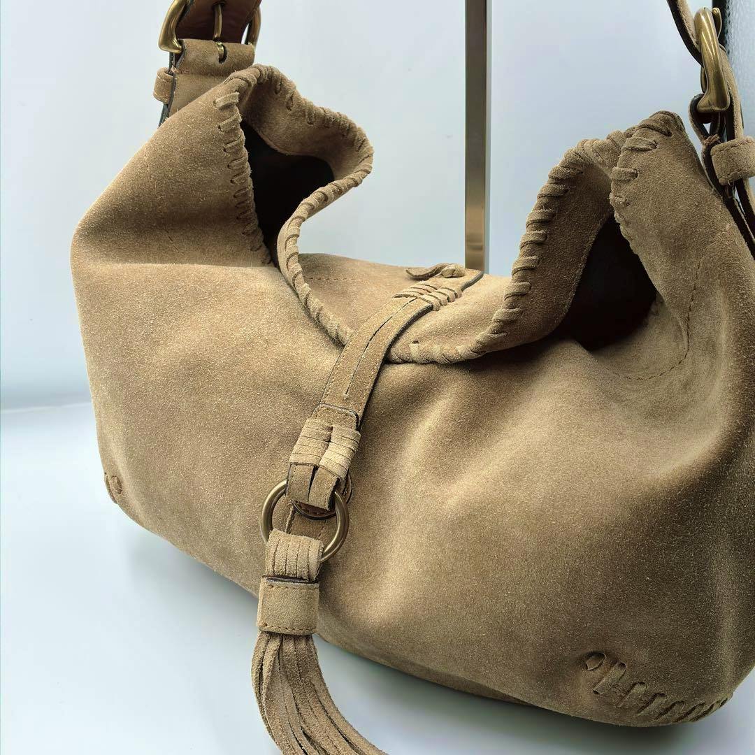 Close-up of a tan suede Coach shoulder hobo bag showing a tassel and whipstitch trim.