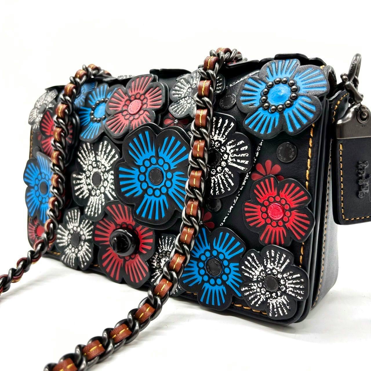 Black leather Coach shoulder bag with multicolor (blue, red, white) floral appliqués and a leather-woven chain strap.