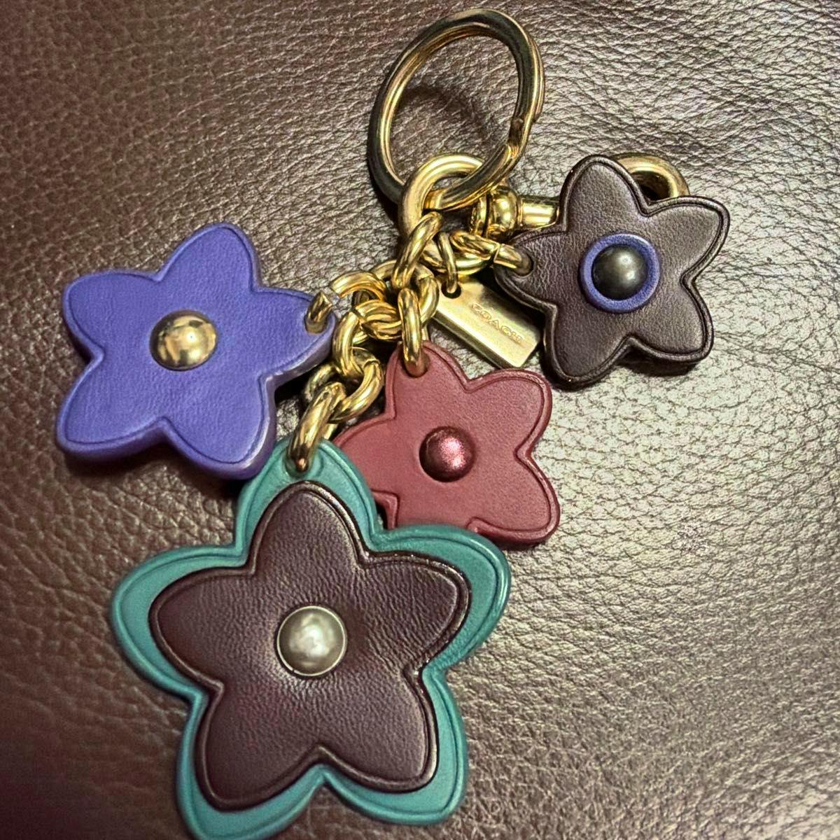 Multicolor COACH leather flower keychain showing four flower-shaped leather charms in purple, teal, burgundy, and brown attached to gold-tone hardware.