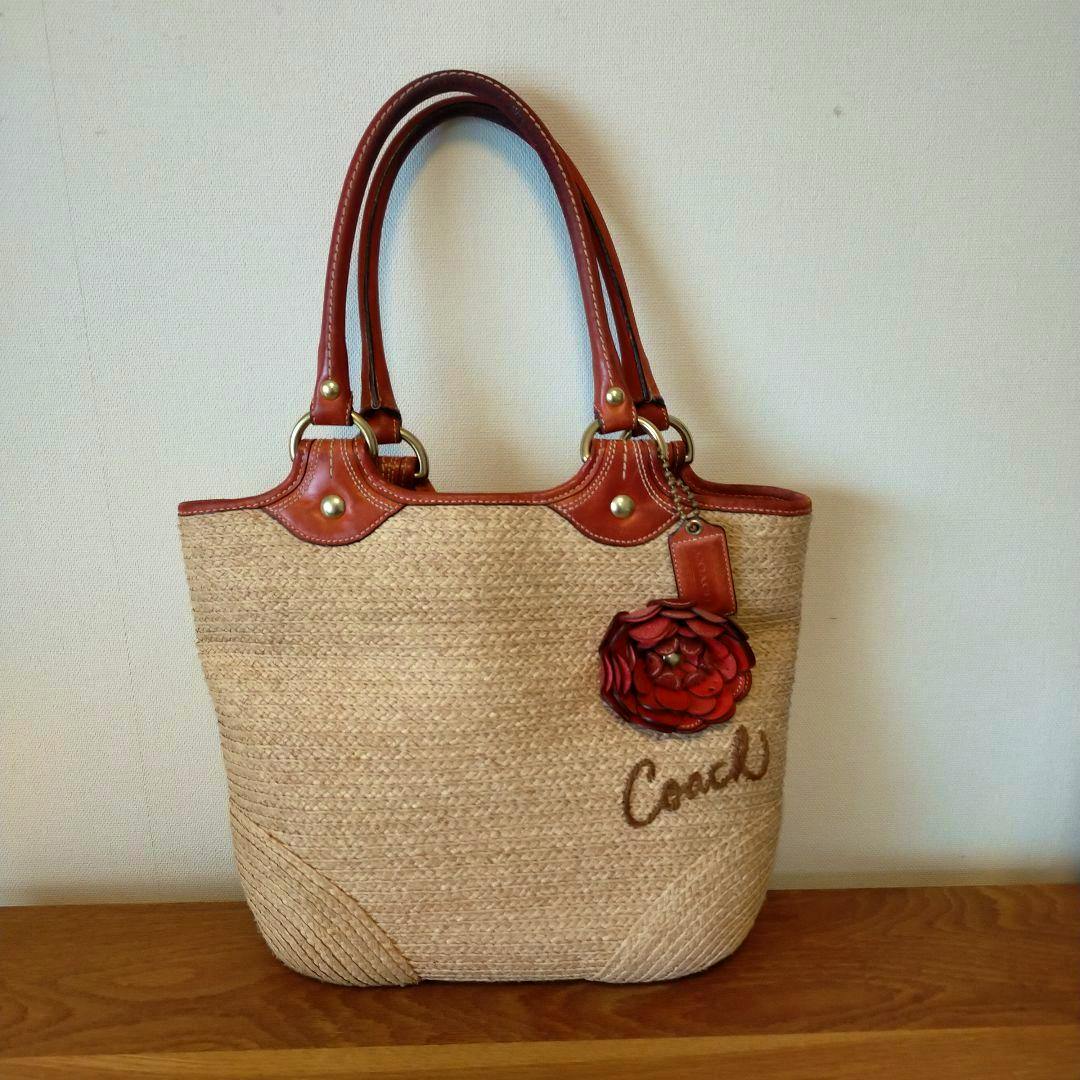 A Coach basket-style canvas bag with brown leather handles and a red flower charm on the front.