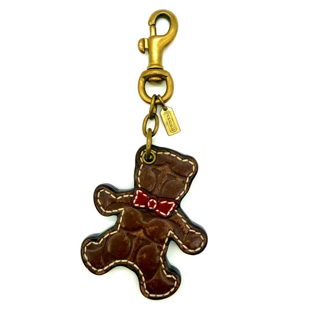 COACH teddy bear bag charm key ring showing a brown teddy-shaped charm with a red bow and a metal swivel clasp.