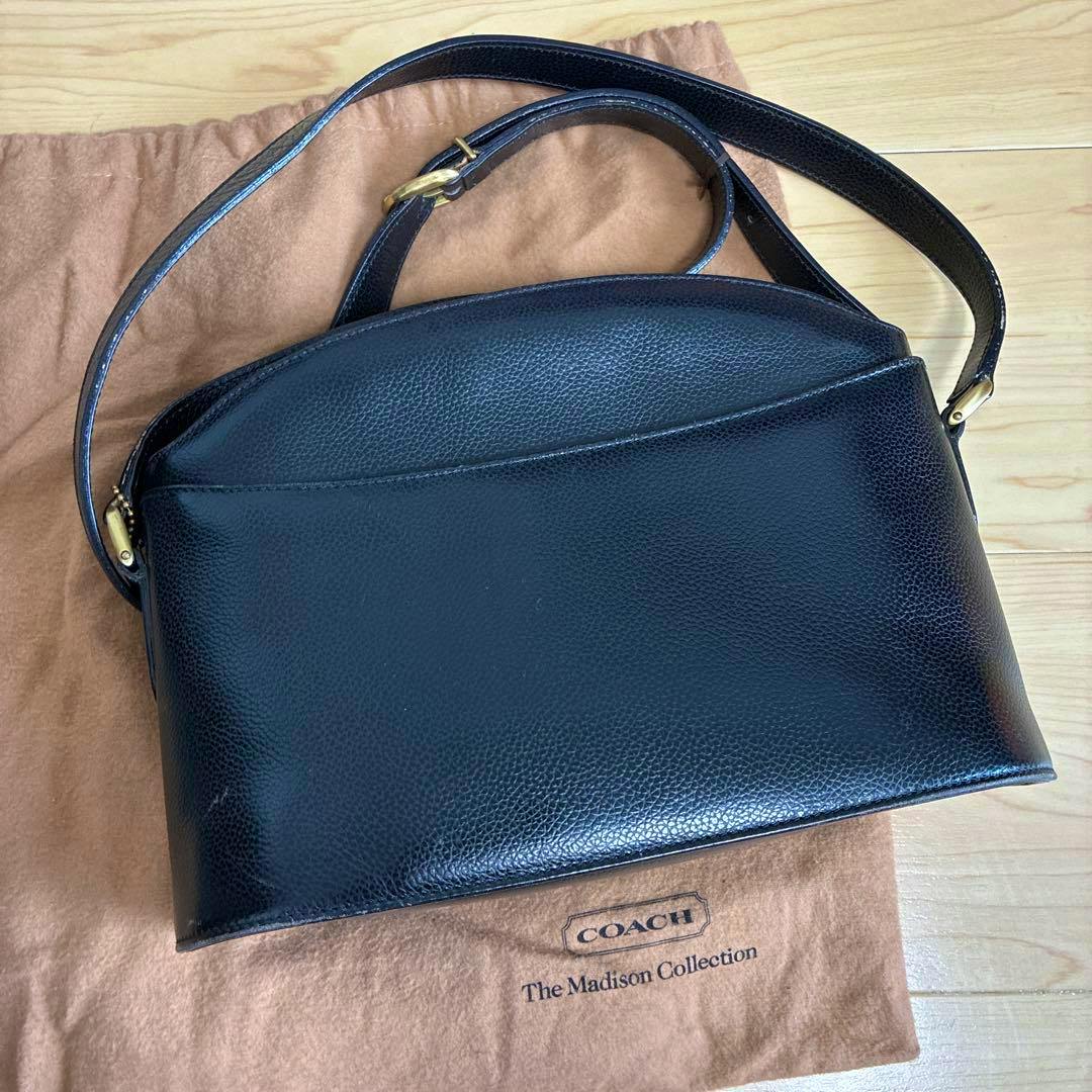 Black leather COACH The Madison Collection shoulder bag shown on a brown dust bag.
