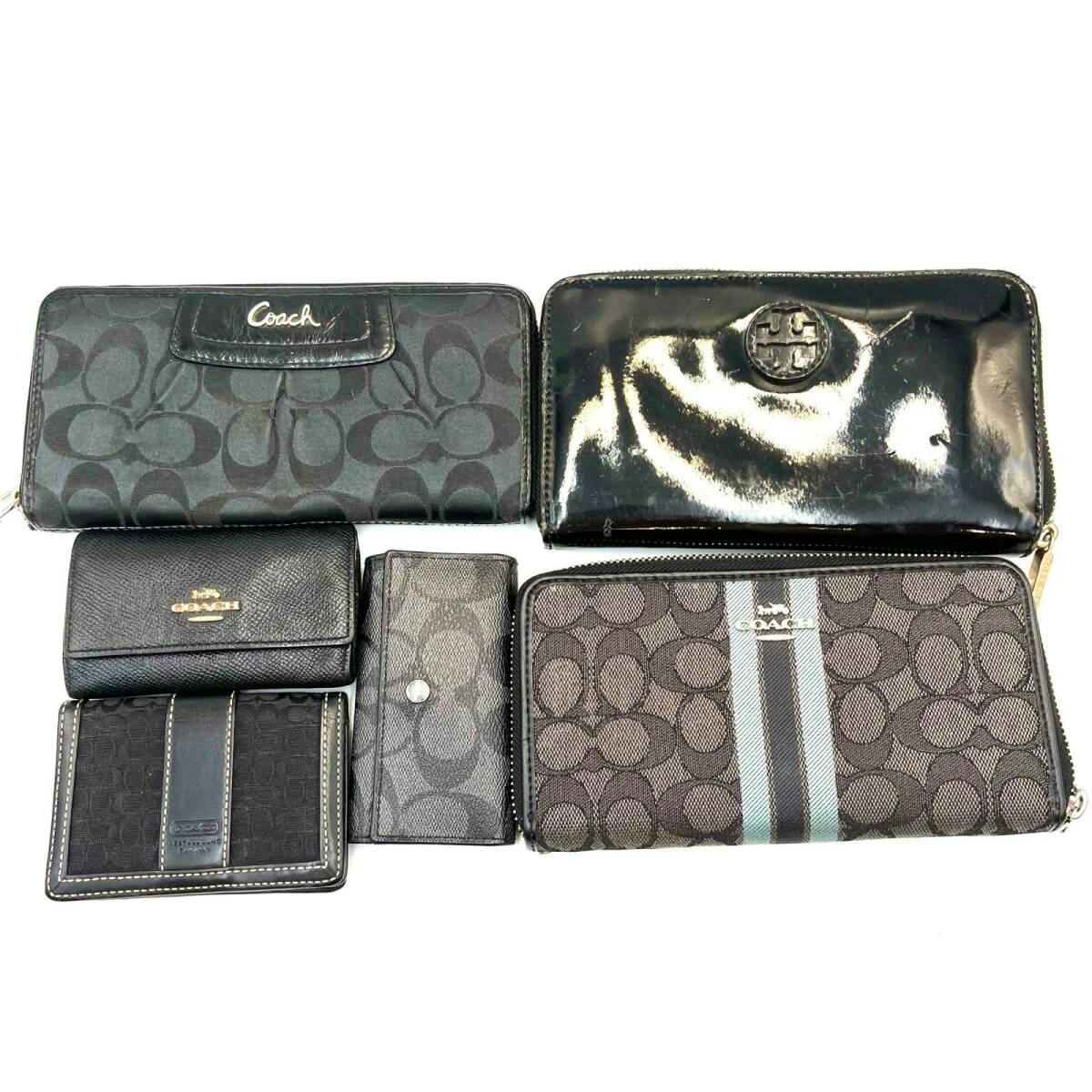 Six black wallets and small cases in Coach and Tory Burch styles arranged on a white background.
