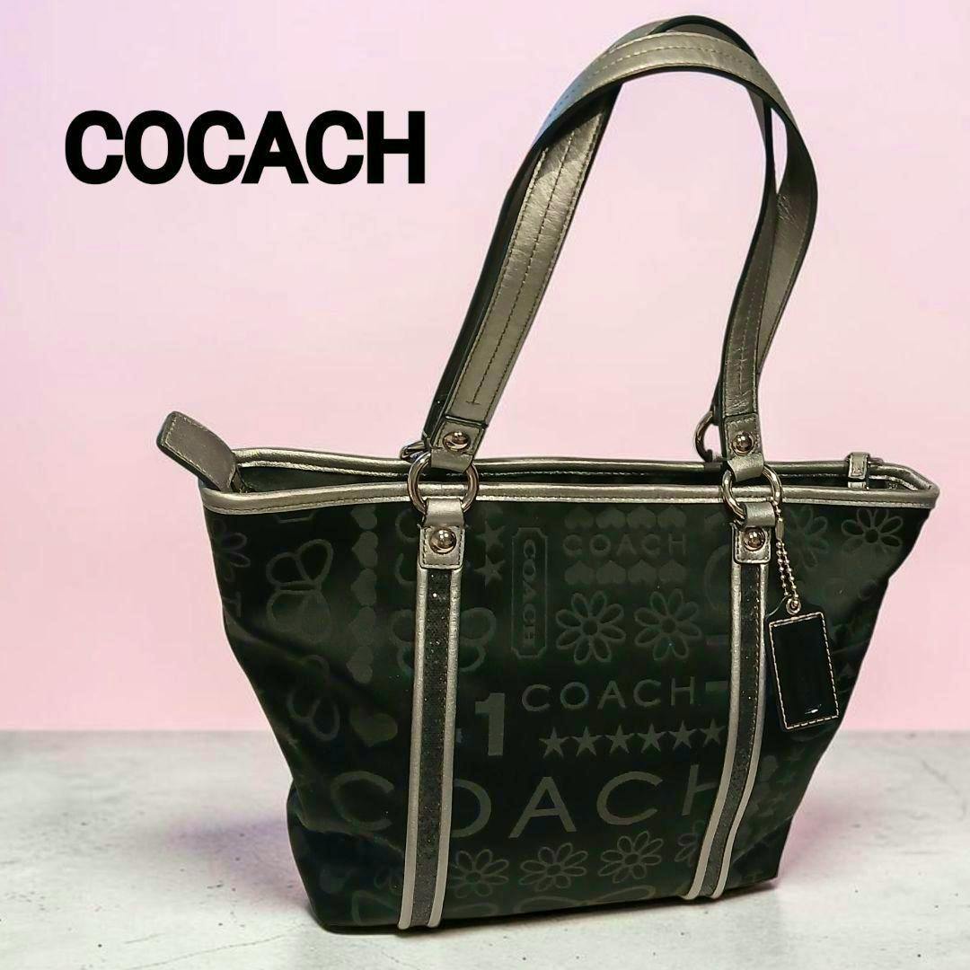 Black Coach canvas tote bag with silver trim and all-over Coach logo pattern shown against a pink background.