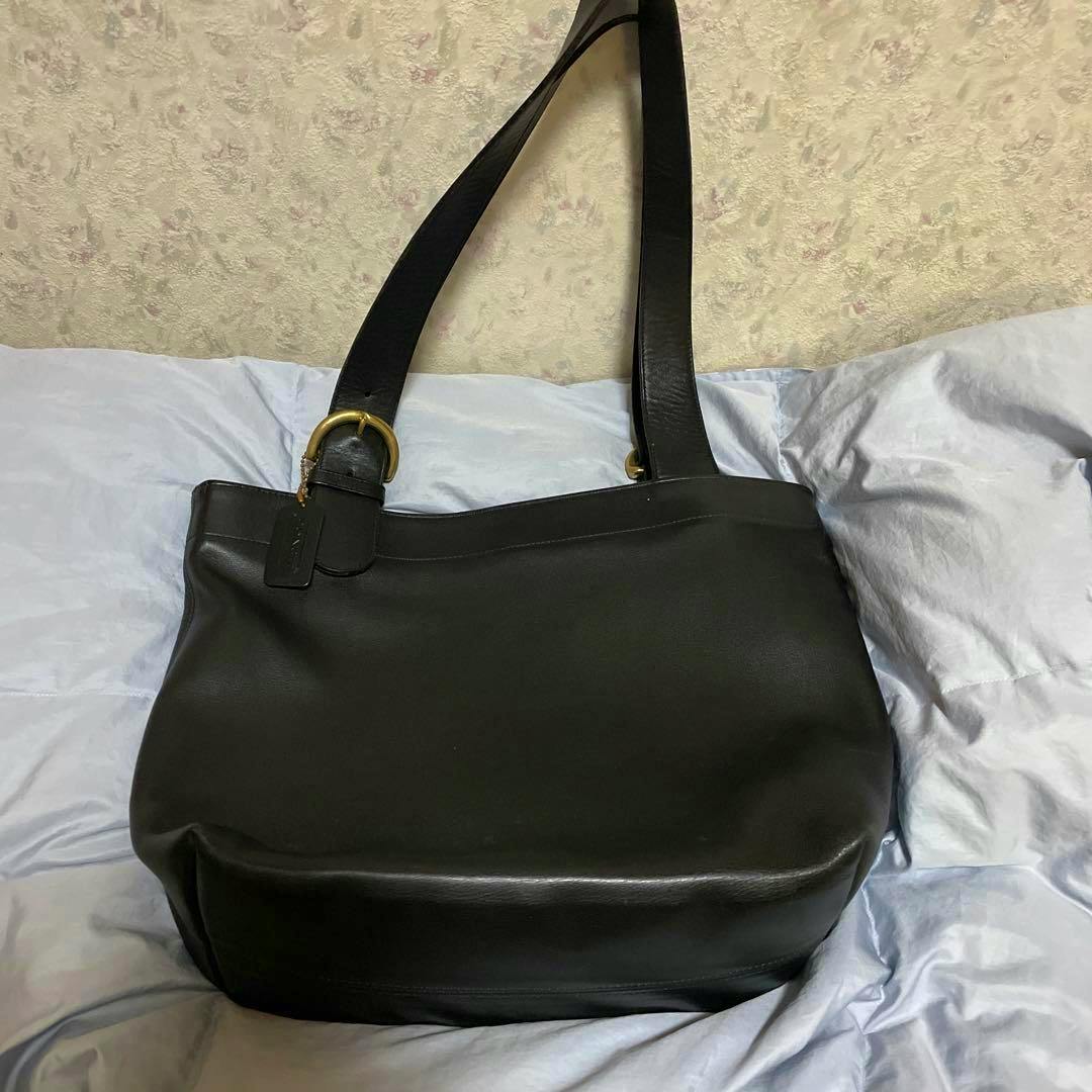 A black Coach tote bag lying flat on bedding showing the front and shoulder straps.