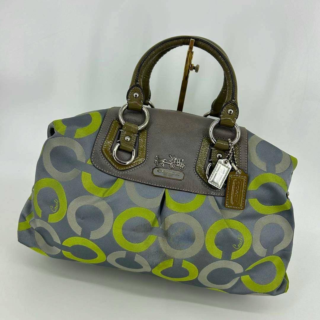 Canvas Coach tote handbag with gray and green circular pattern, brown leather trim, top handles, and metal logo tag on a white background.