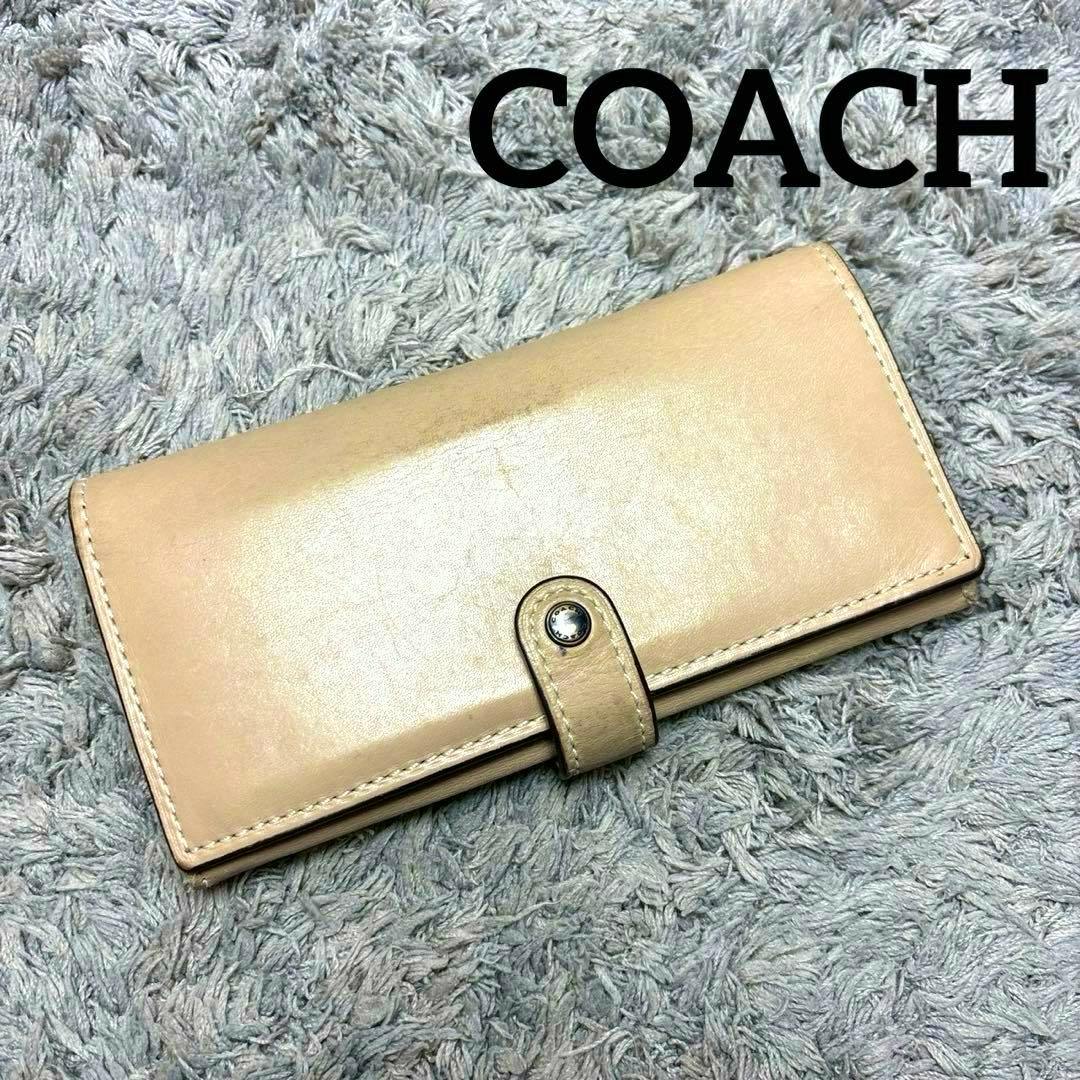Beige COACH trifold long leather wallet closed and photographed on a gray shag rug.