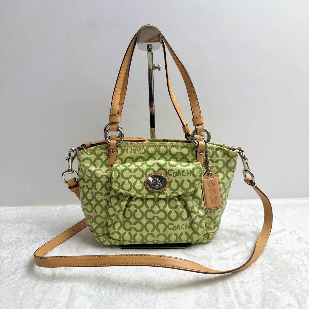 Green Coach canvas shoulder bag with repeated C pattern, tan leather straps, a front turn-lock pocket, and a detachable long strap.