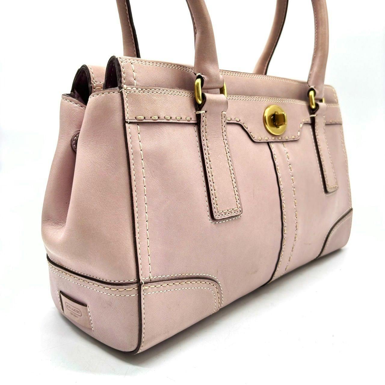 Pink Coach leather turn-lock handbag with gold hardware shown in a three-quarter view.