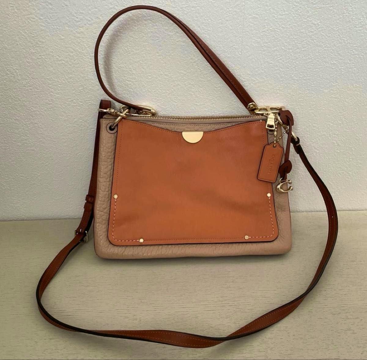Front view of the COACH 2WAY shoulder bag (ターンブロック) showing a tan front pocket, beige leather body, and brown shoulder strap with gold hardware.