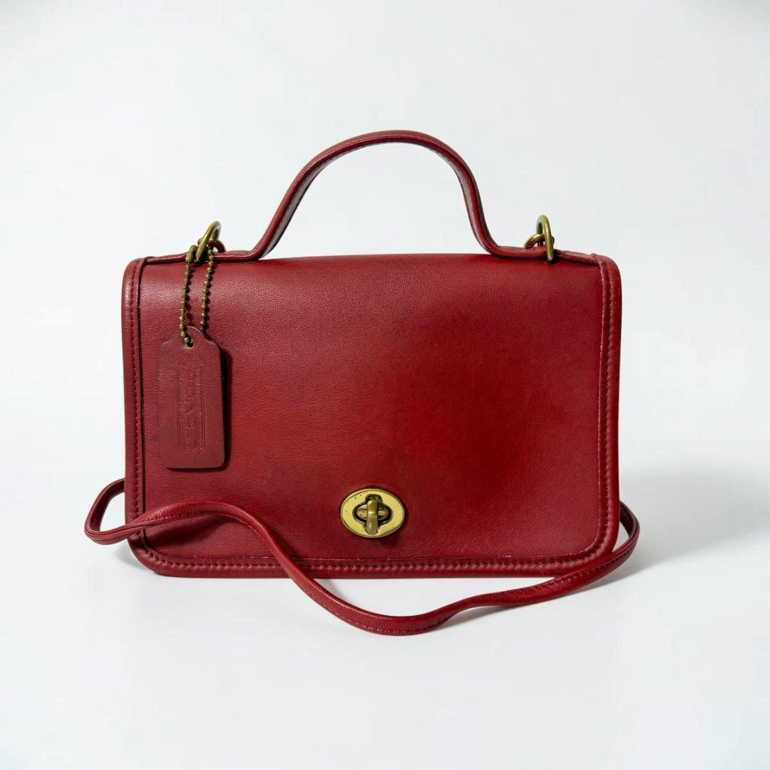 Red COACH turn-lock 2WAY shoulder bag shown front-on with top handle, shoulder strap, and brass turn-lock closure on a white background.