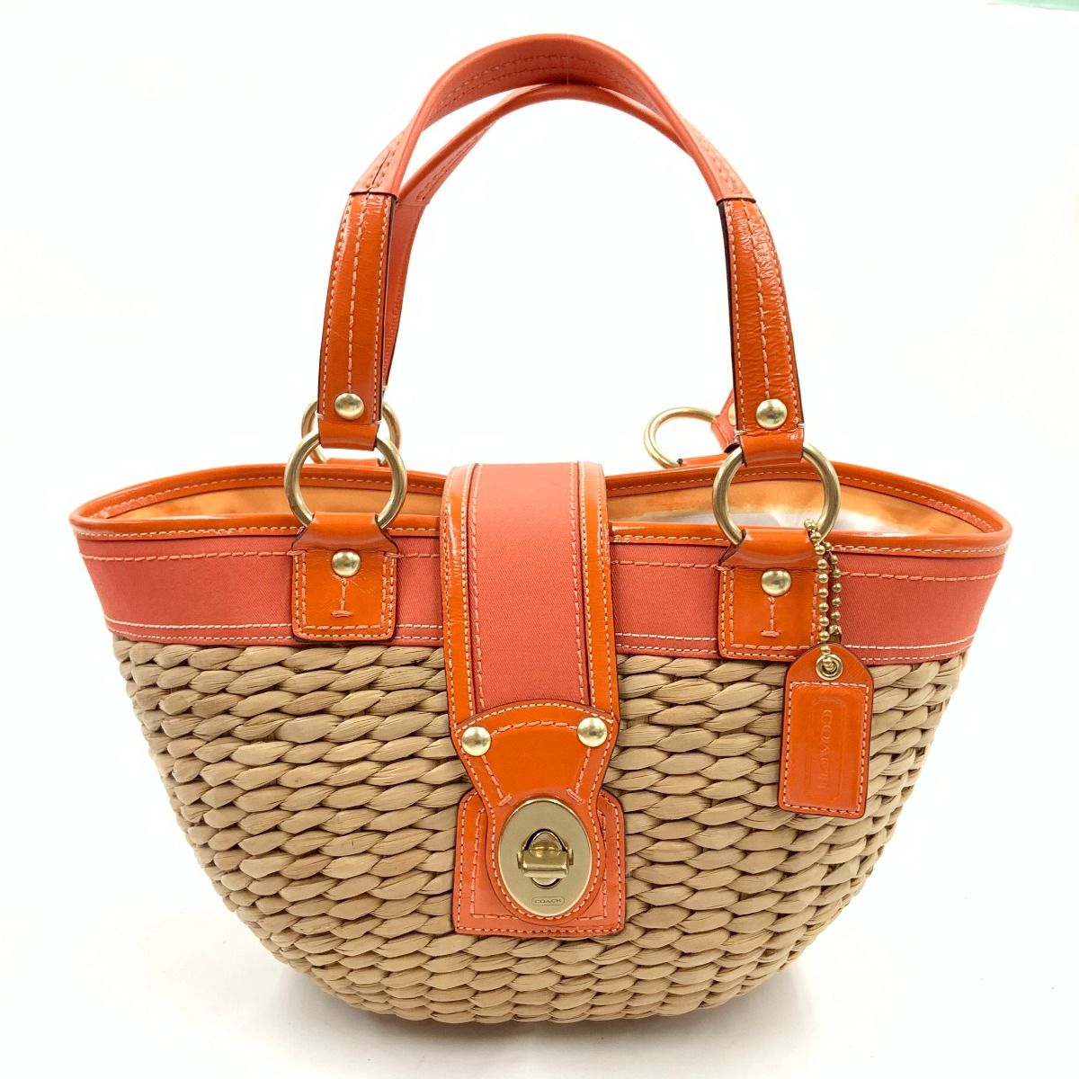 Orange Coach turn-lock basket tote bag with woven body, orange leather trim and handles, and a front turn-lock closure.