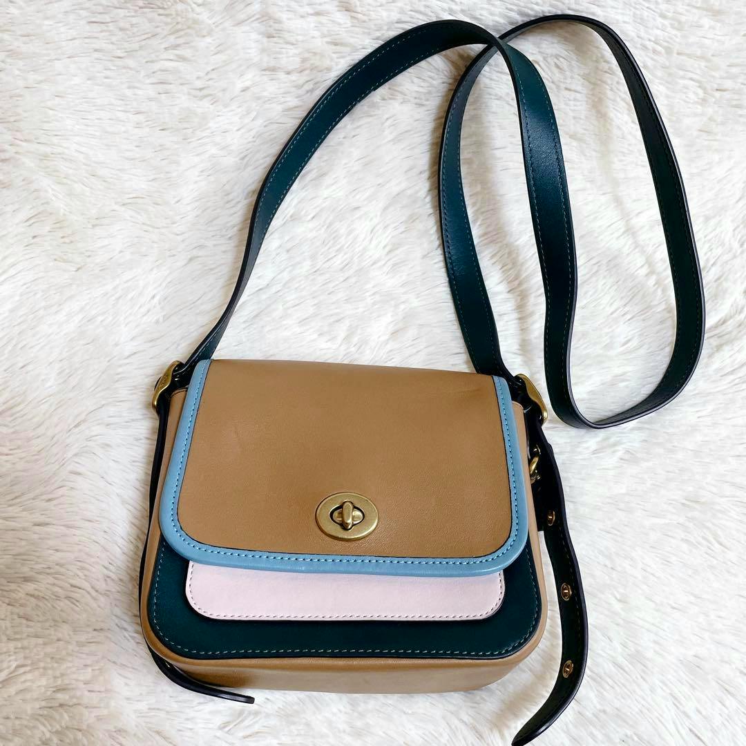 Multicolor Coach turn-lock camera shoulder bag in leather shown on a white fur background.