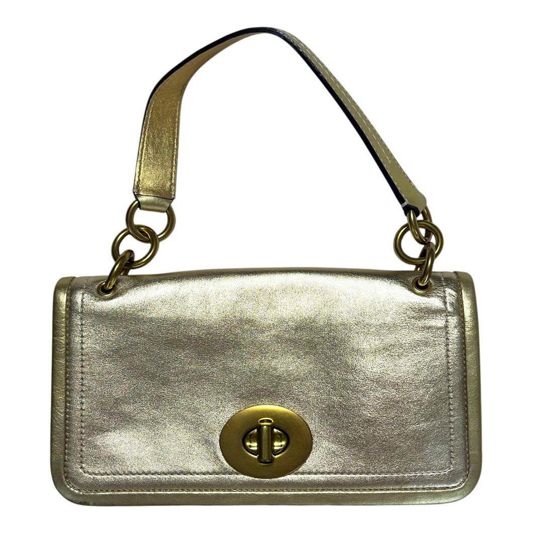 Front view of a metallic gold Coach handbag showing its short handle and oval turn-lock closure.