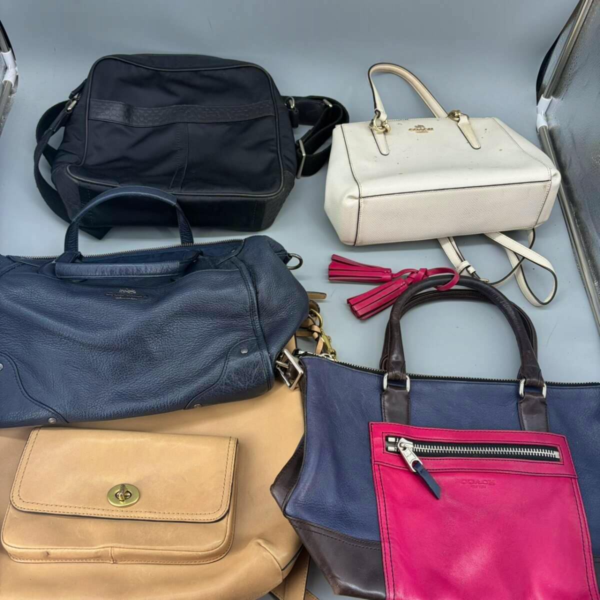 Several COACH bags in different colors arranged flat on a surface, showing handles and pockets.