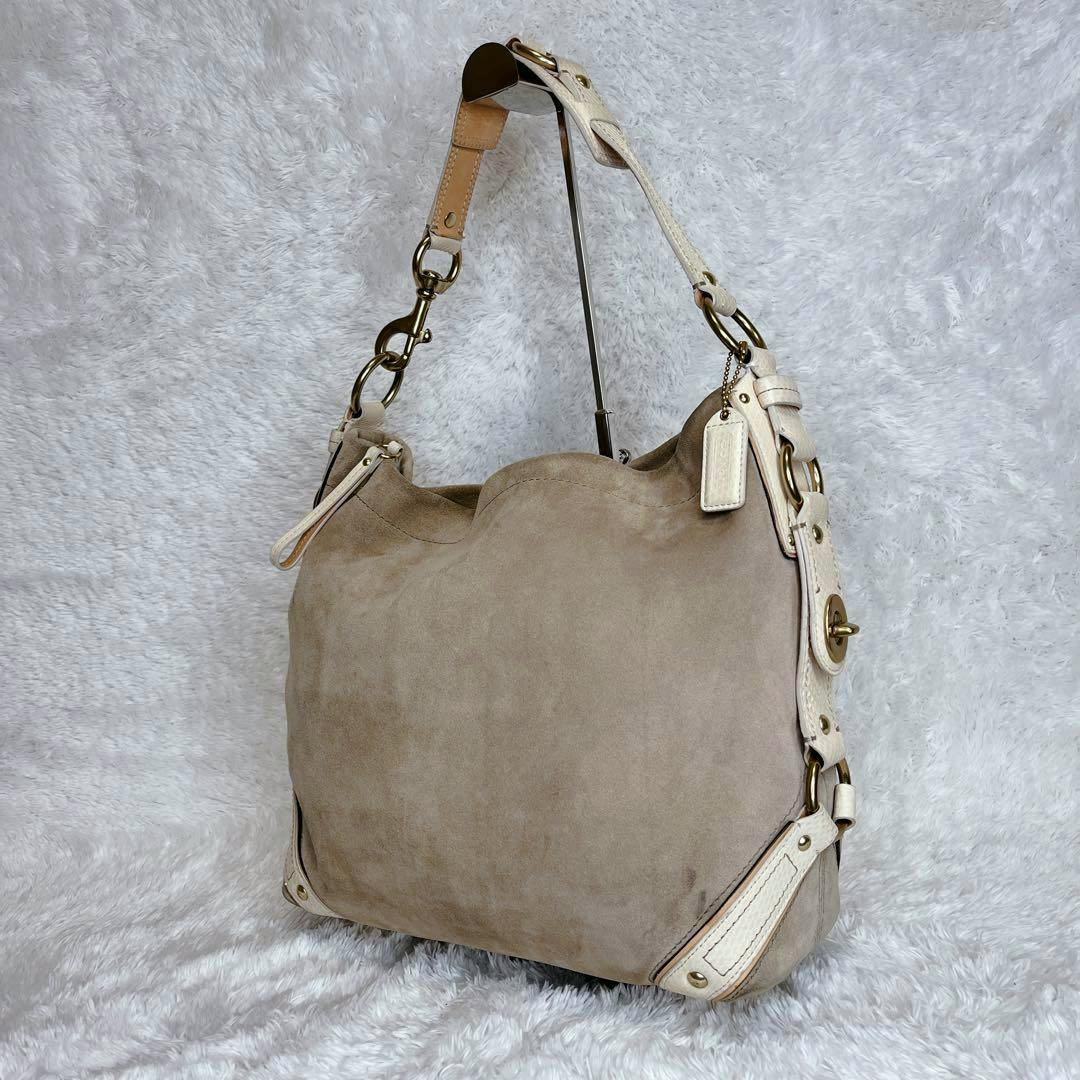 Beige suede COACH one-shoulder bag with light leather trim and metal hardware on a white plush background.