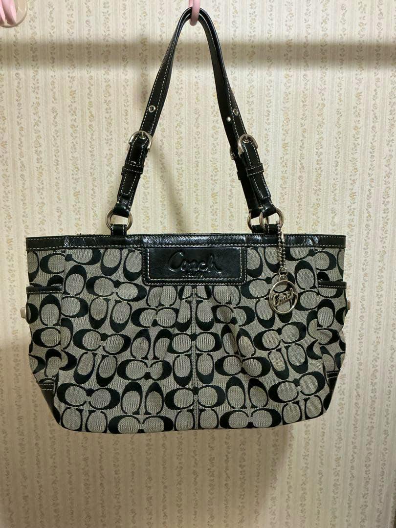 Front view of a Coach canvas tote bag with signature C pattern, black leather trim, and a Coach hanging charm.