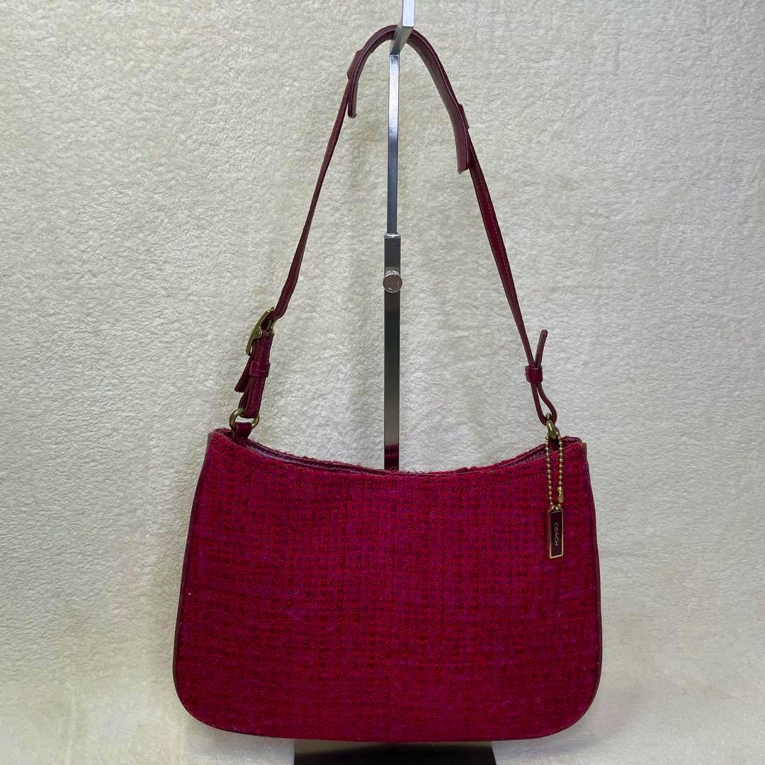 Red tweed Coach one-shoulder bag with a leather strap hanging on a display stand.