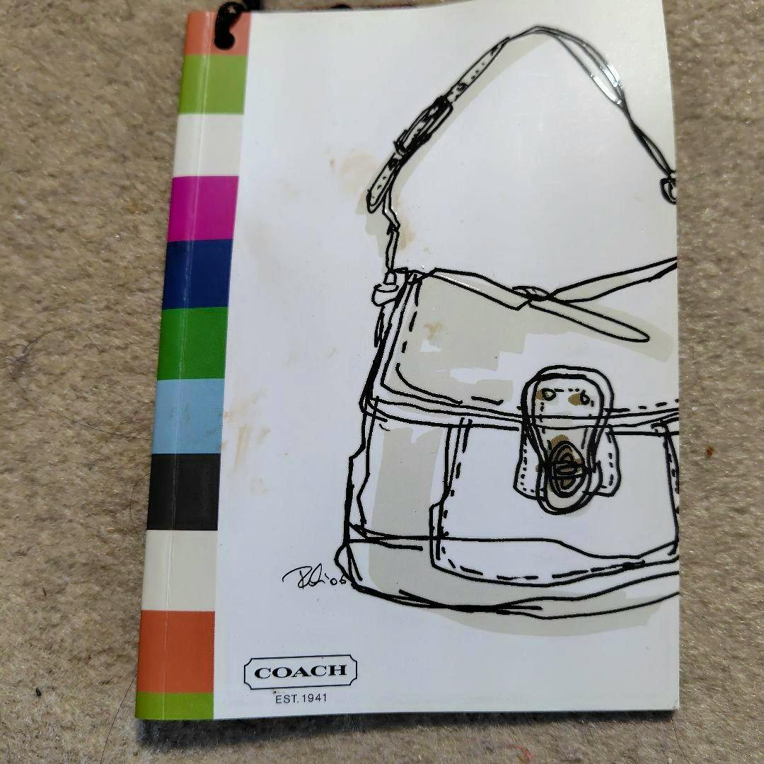 Front cover of the COACH notebook showing a line-drawn bag illustration, multicolored spine stripes, and the COACH logo.