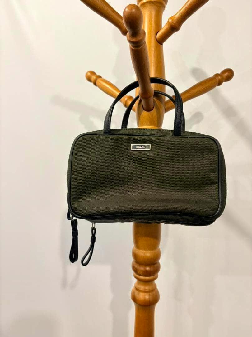 Khaki COACH vanity bag makeup pouch with two short handles hanging on a wooden stand.