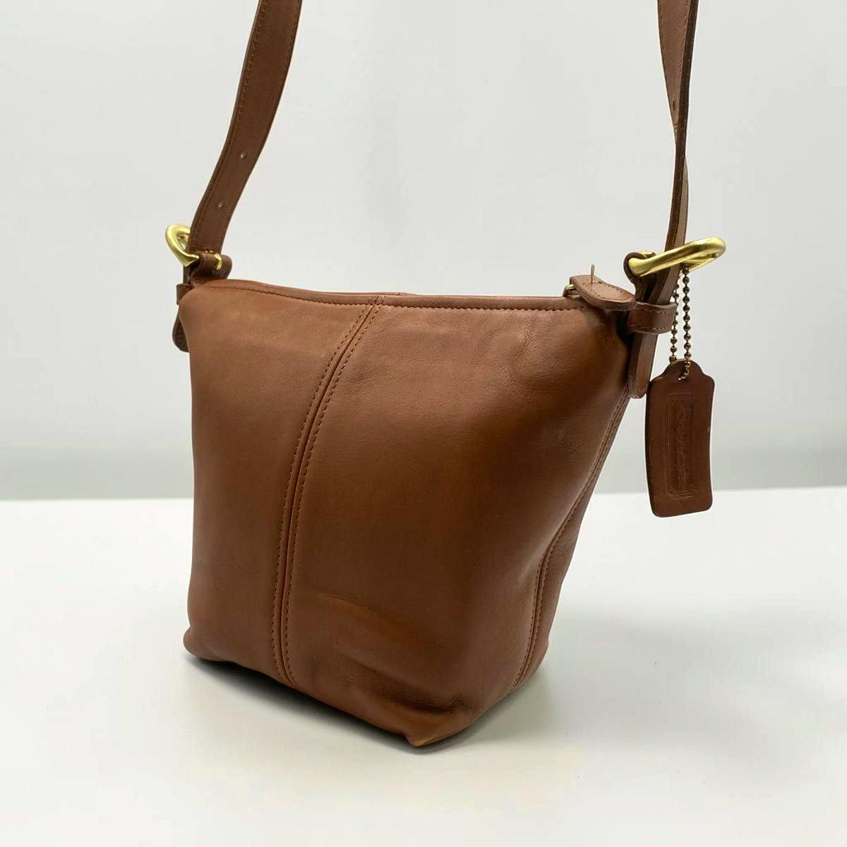 Brown leather Coach bucket-style shoulder bag with strap and leather tag on a white surface.