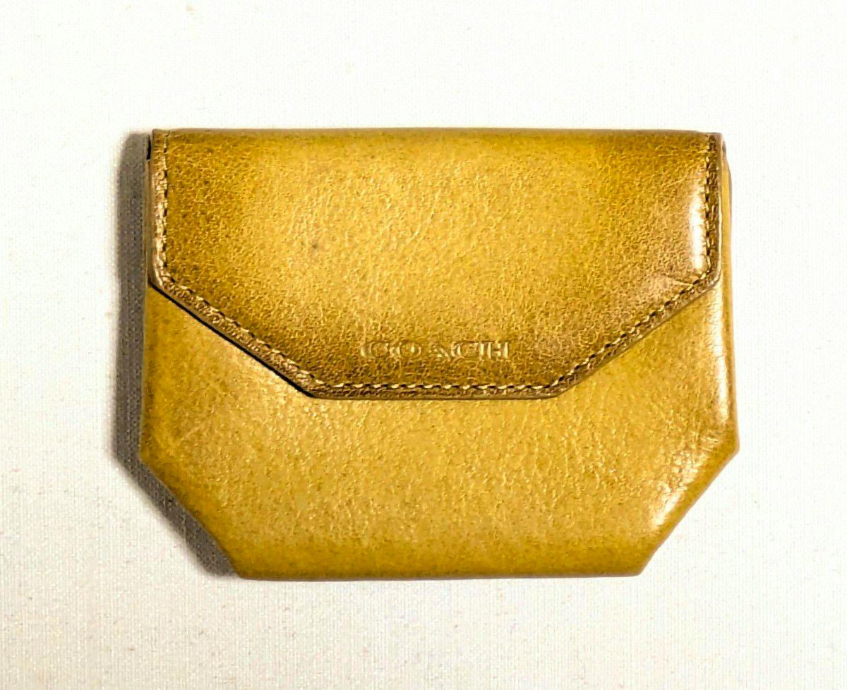 Front view of a tan leather COACH coin case on a white background.