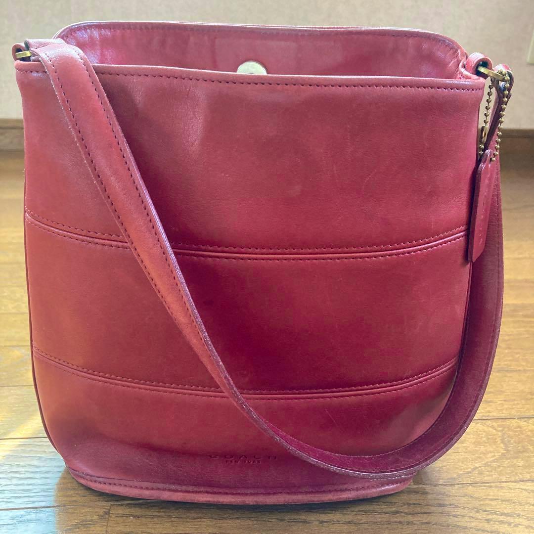 Front view of a red Coach vintage cow leather shoulder bag with a shoulder strap on a wooden floor.
