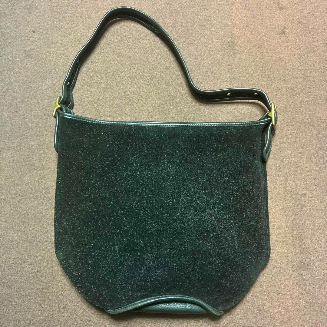 Front view of a suede Coach shoulder bag with leather trim and a single adjustable strap laid flat on a surface.