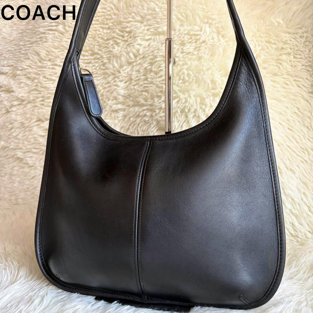 Front view of a black COACH leather shoulder bag displayed on a cream fur background.