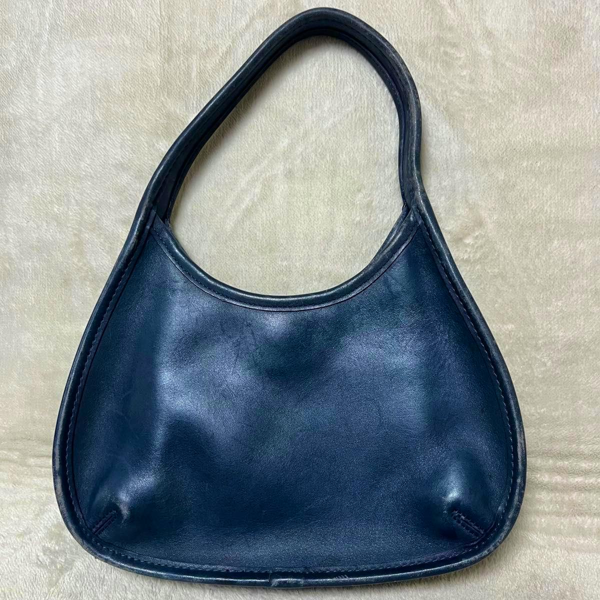 Front view of a COACH navy leather one-shoulder handbag laid flat on a light background.
