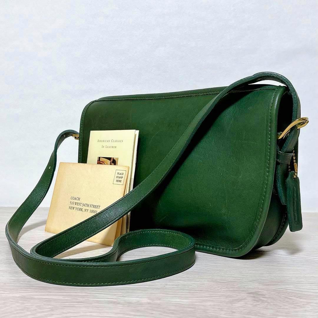 Green leather Coach vintage shoulder bag with long strap shown on a light surface with small booklets beside it.