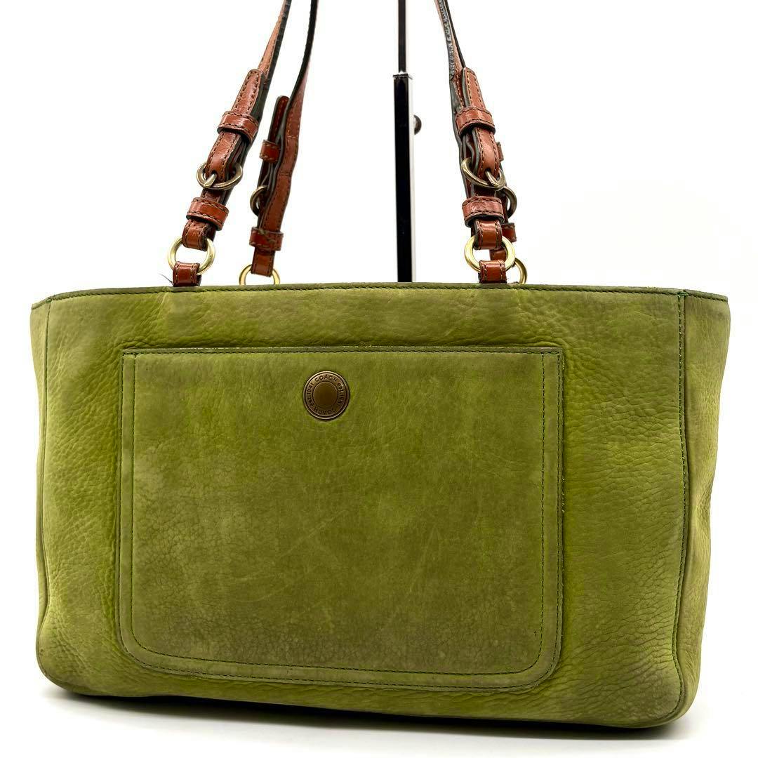 Front view of COACH green nubuck handbag showing an exterior pocket and brown leather shoulder straps on a display stand.