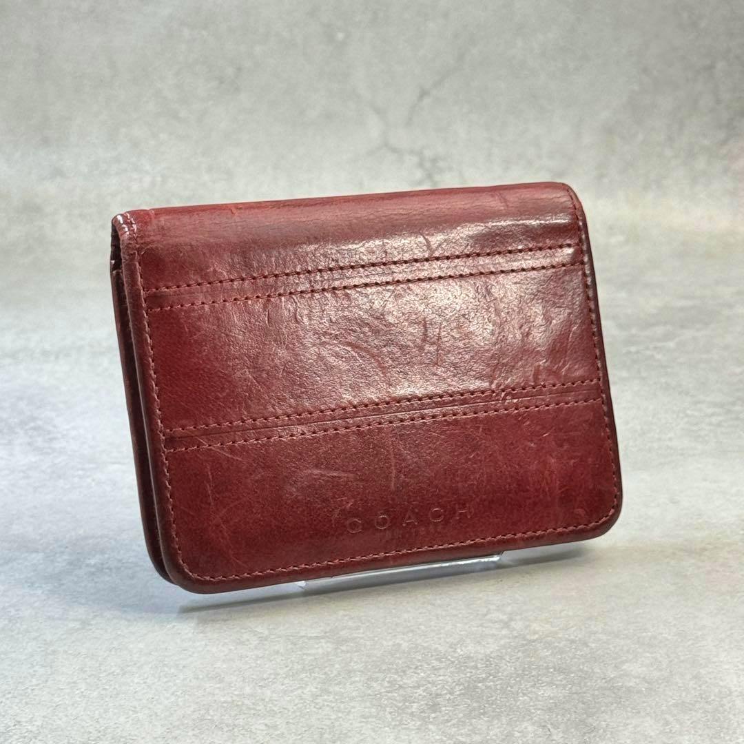 Bordeaux leather Coach vintage bi-fold wallet shown closed at an angled front view on a small stand.