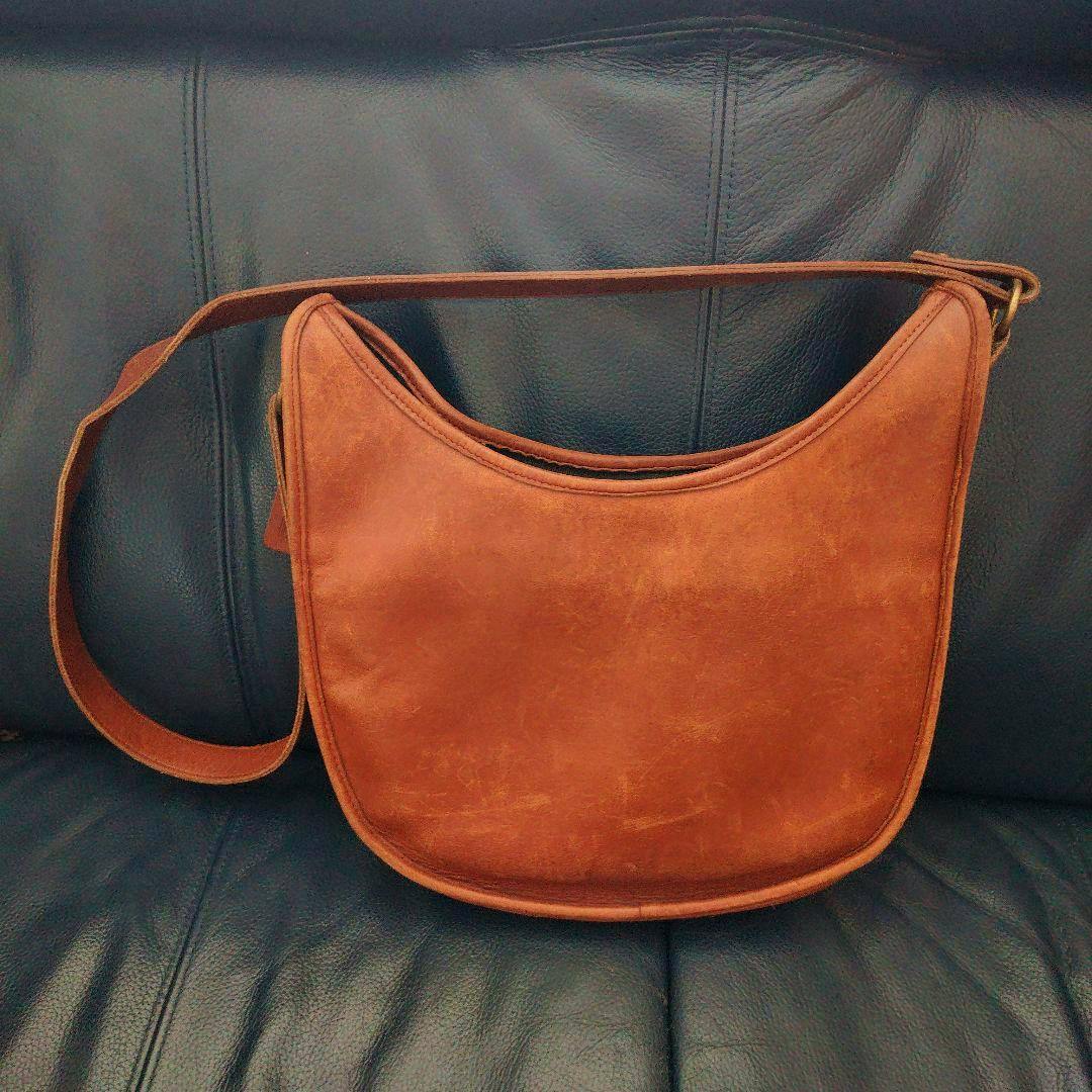 Brown leather Coach shoulder bag shown front-facing on a dark leather sofa.