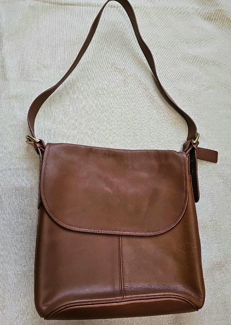 Brown leather shoulder bag with a front flap and single shoulder strap laid flat on a light background.