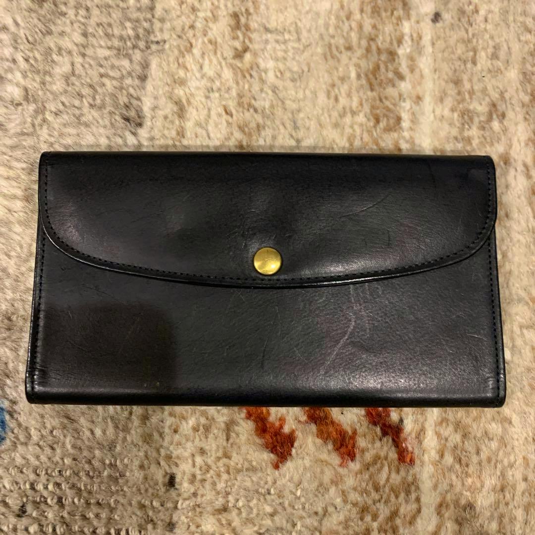 Front view of the black cow leather long wallet showing a flap with a round brass snap closure.