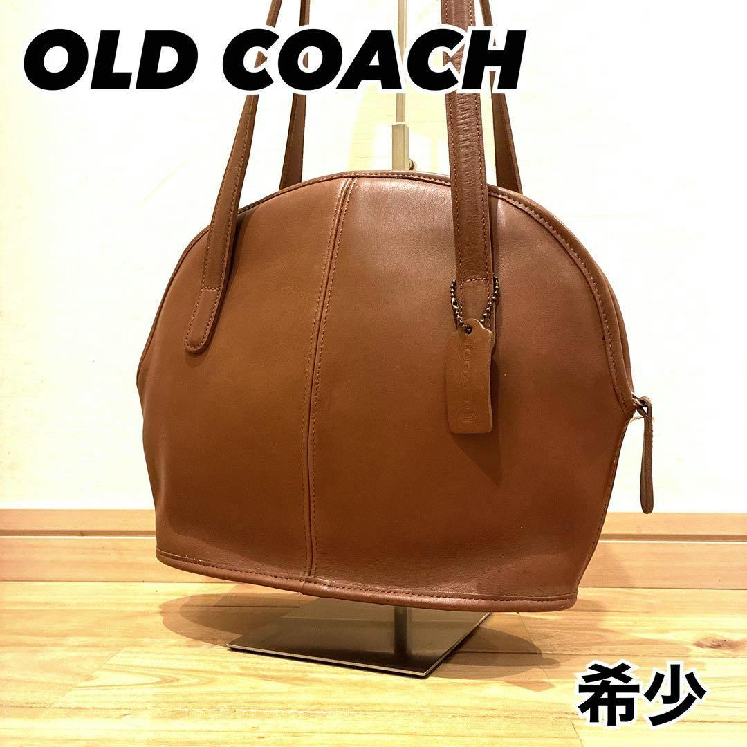 Brown Coach leather shoulder bag on a stand, showing the full bag with handles and a leather Coach tag.