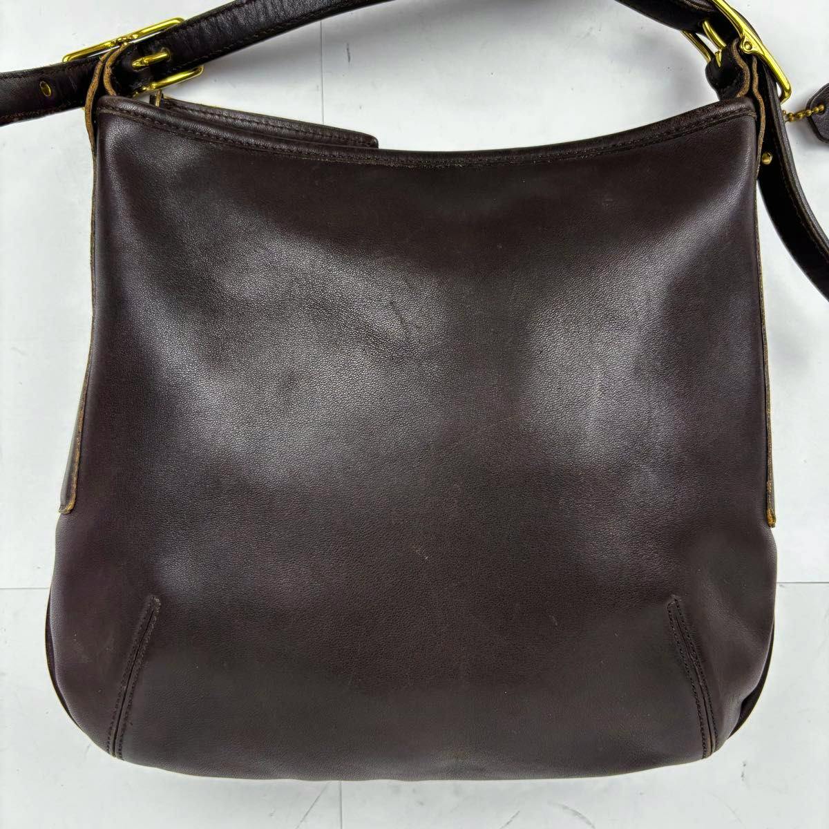 Dark brown leather COACH shoulder bag laid flat showing the front and strap.