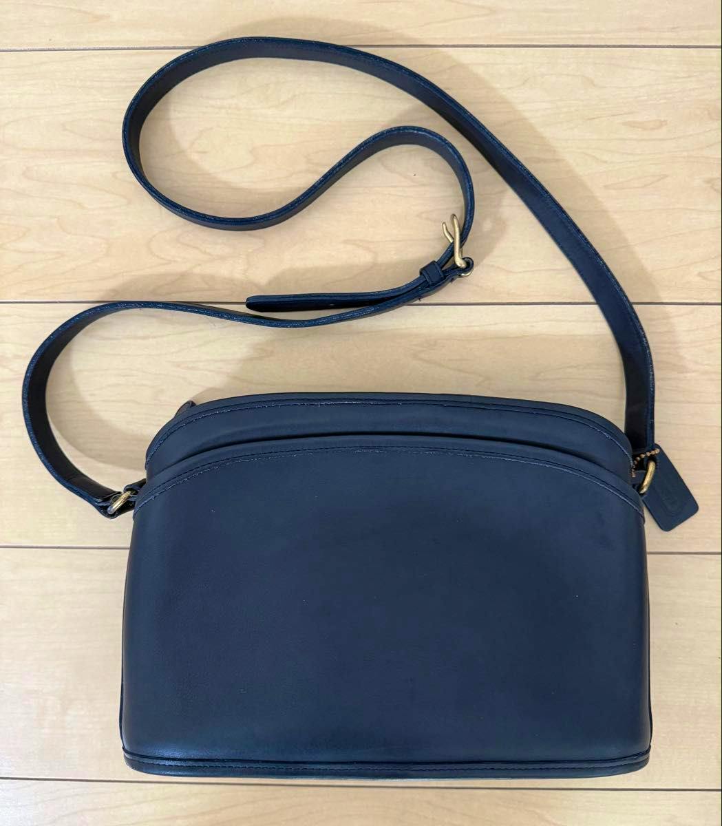 Navy-blue leather COACH shoulder bag with long strap laid flat on a wooden floor.