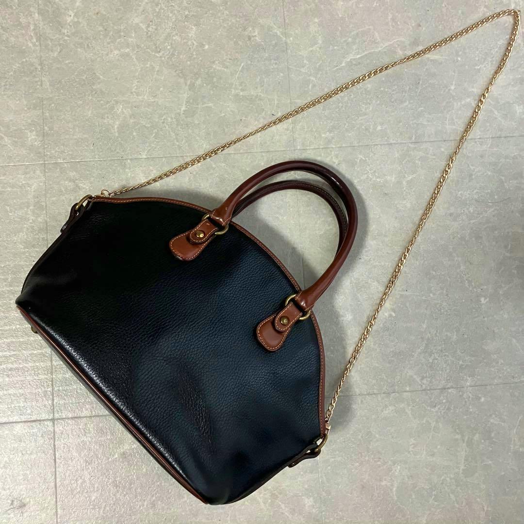 Black leather Coach vintage Sheridan shoulder handbag with brown leather handles and a gold chain strap laid flat on the floor.