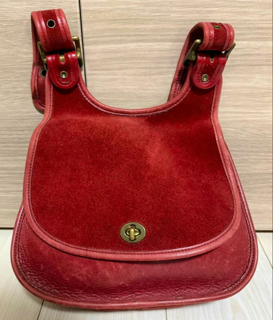 Front view of a red suede and leather Coach shoulder bag with flap and turn-lock closure.