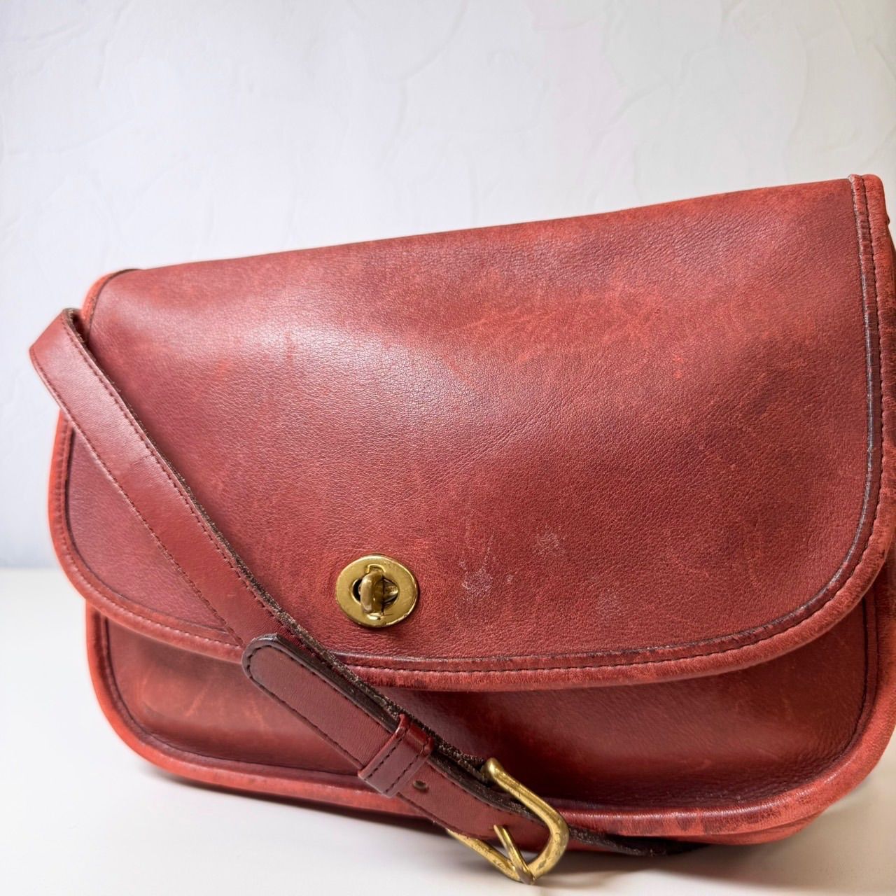 Red vintage Coach glove-tanned leather shoulder bag with a turn-lock closure, adjustable strap, and brass hardware.