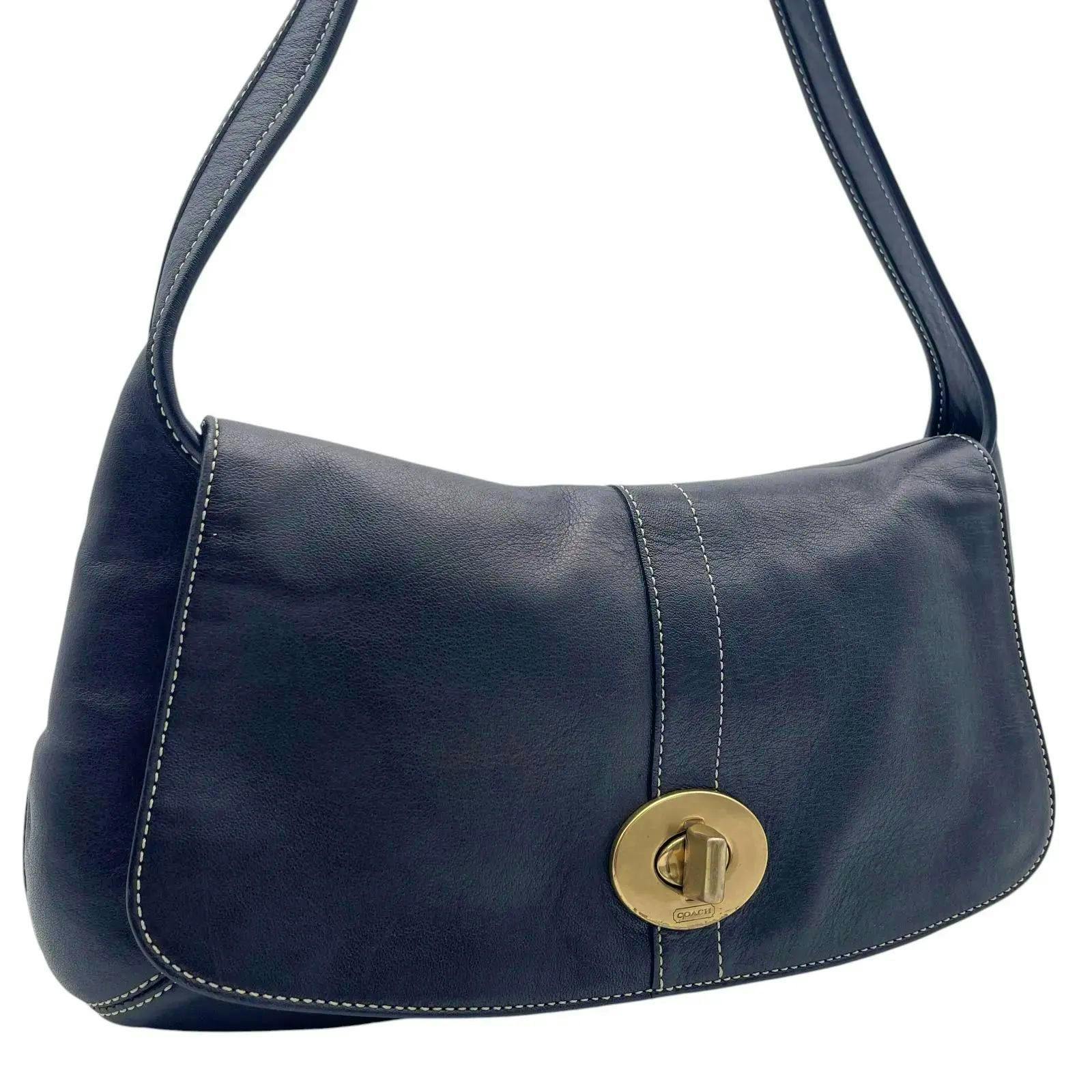Front of a black Coach leather shoulder bag with a gold turn-lock and white contrast stitching.