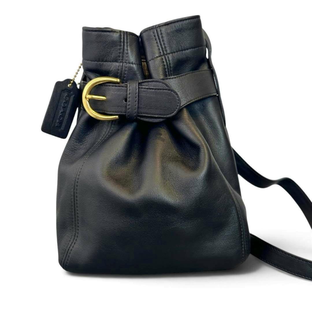 Front view of a black COACH leather shoulder bag showing a gold buckle and leather hang tag.