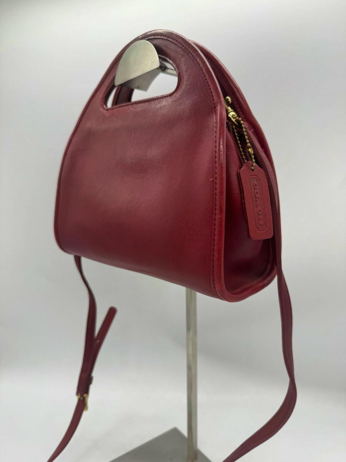 Red Coach leather 2-way hand bag shown from a side angle with handle cutout, shoulder strap, and Coach hang tag.